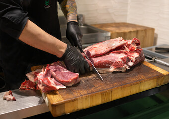 Butcher cuts the meat with a knife on a wooden board. Cutting and preparation of farm meat products