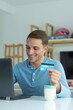 © Carlos Daniel Ibañez - handsome young blond man holding with his hand a credit card shopping online, with his laptop smiling at home