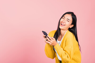 Poster - Happy Asian portrait beautiful cute young woman excited laughing holding mobile phone, studio shot isolated on pink background, female using funny smartphone making winner gesture