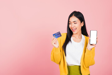 Wall Mural - Happy Asian portrait beautiful cute young woman excited smiling hold mobile phone and plastic debit credit bank card, studio shot isolated on pink background, female using smartphone online shopping