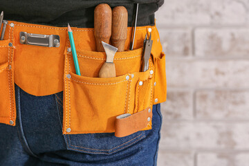 Male carpenter with tool belt near brick wall, closeup