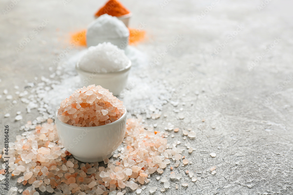 Bowls with different salt on grey background, closeup