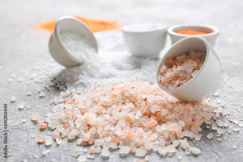 Bowls with different salt on grey background, closeup
