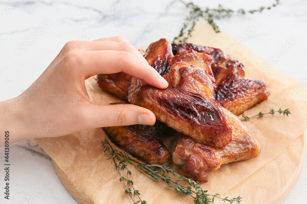 Woman eating roasted chicken wings on light background