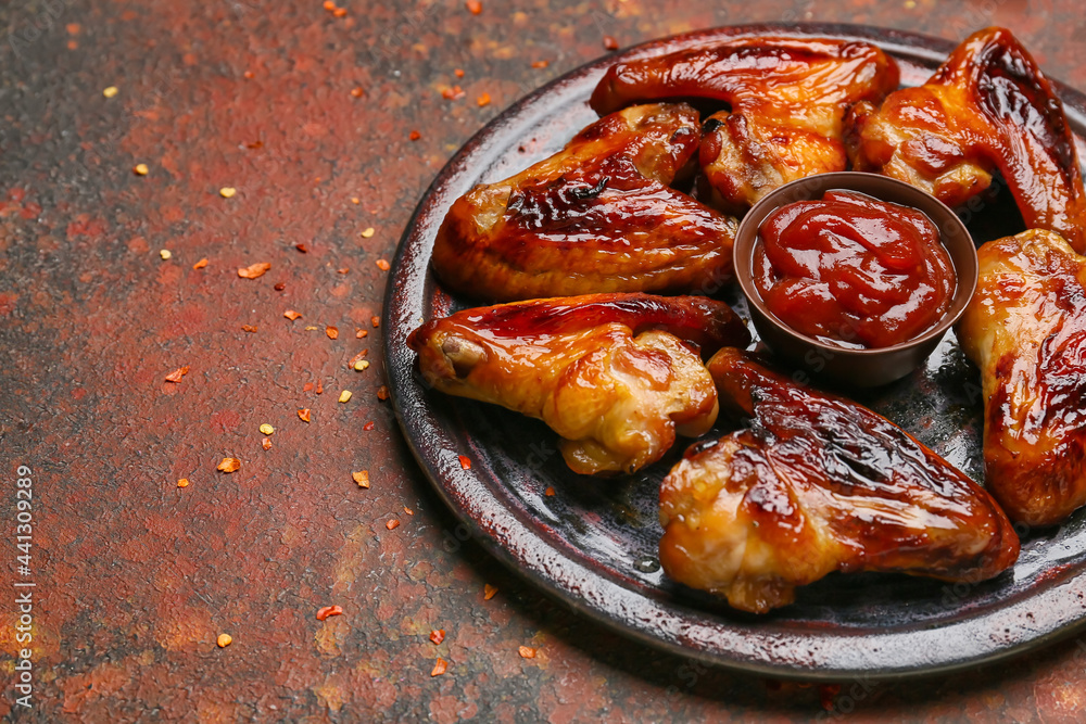 Board with roasted chicken wings and sauce on grunge background