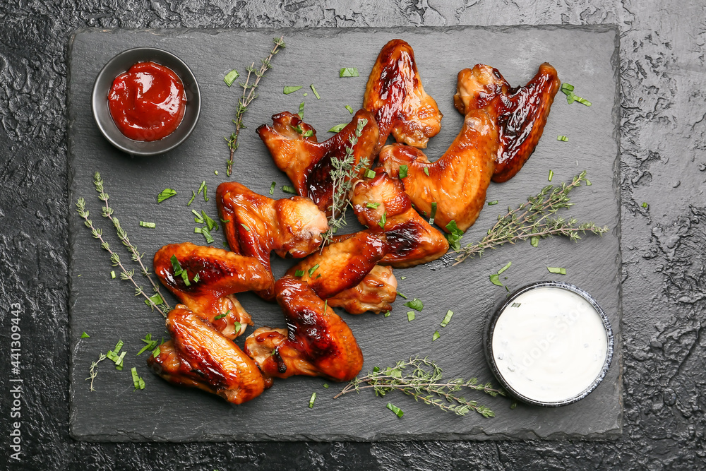 Roasted chicken wings and sauces on dark background