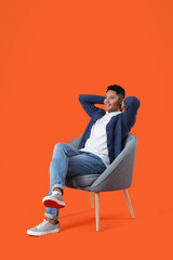 Sticker - Young African-American guy sitting in armchair on color background