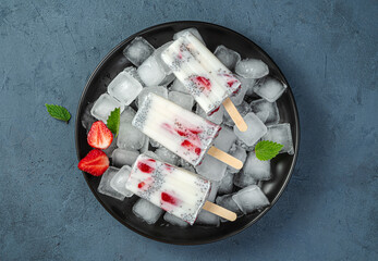 Three ice creams with strawberries and chia seeds on ice cubes in a black plate on a blue background