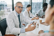 © Seventyfour - Portrait of white haired senior doctor talking to colleagues at meeting table during medical conference