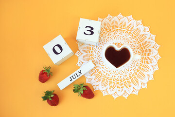 Calendar for July 3 : cubes with the numbers 0 and 3, the name of the month of July in English, a cup of tea in the shape of a heart on a white openwork napkin, strawberries on a yellow background