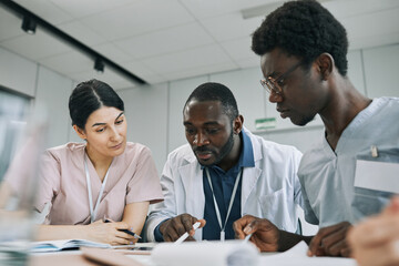 Multi-ethnic group of doctors looking at X-ray images on display during medical council in conference room