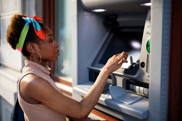 Beautiful african women using ATM machine. Attractive young woman withdrawing money from credit card at ATM.