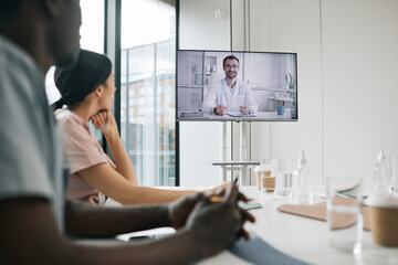 Wall Mural - Portrait of male doctor on screen speaking to group of colleagues during medical conference, copy space