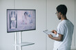 © Seventyfour - Back view at African-American doctor speaking to female expert by video call in clinic, copy space