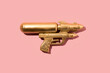 Gold hipster watergun or handgun on pink pastel background. Minimal flat lay concept.