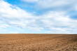Plowed brown field and white clouds on blue sky.cloudy sky over brown field.Spring summer day.