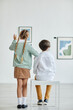 © Seventyfour - Vertical back view at boy and girl looking at paintings in art gallery