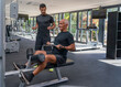 Elderly man, athletic physique is exercising on a exercise machine, with a fitness trainer. In gym.