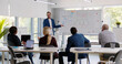 © TommyStockProject - Man presenting report on whiteboard to diverse colleagues in business center