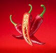 Fresh red chilli peppers and cross sections of chilli pepper with seeds floating in the air.