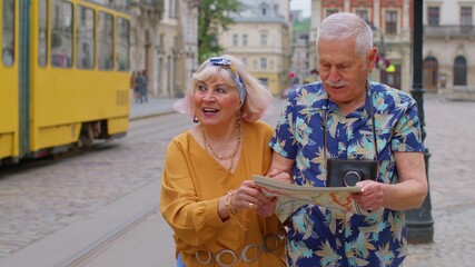 Wall Mural - Senior old good looking stylish tourists man and woman having a walk and look for way using paper map in city Lviv, Ukraine. Elderly grandmother, grandfather enjoying traveling together. Mature family