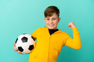 Little redhead boy isolated on blue background with soccer ball celebrating a victory