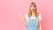 Pretty Red Head Woman Looking Surprised And Shocked, With Jaw Dropped Holding An Object