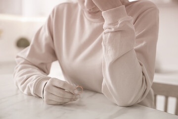 Wall Mural - Woman holding wedding ring at table indoors, closeup. Cheating and breakup