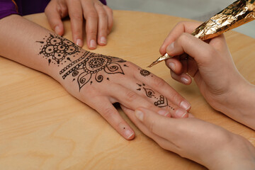 Wall Mural - Master making henna tattoo on hand at wooden table, closeup. Traditional mehndi