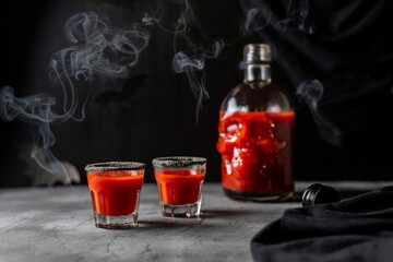 Tomato cocktail in a skull-shaped bottle and glasses with smoke. Drink for Halloween party