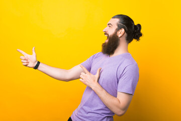 Happy excited bearded man pointing away at copy space with two fingers isolated over yellow background