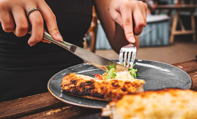 Wall Mural - woman hands with knife and fork cutting pizza on table in cafe outdoor