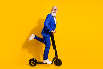 Wall Mural - Full body profile photo of funny grey beard aged man ride scooter wear spectacles blue suit isolated on yellow background