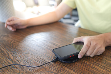 Wall Mural - Charging mobile phone battery with wireless device in the table. Smartphone charging on a charging pad. Mobile phone near wireless charger.