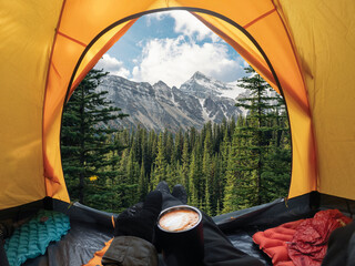 traveler lying and holding coffee cup in yellow tent and enjoy the view of forest and mountain in na