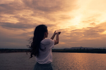 Young woman standing outstretched hands praying for blessing with sunset sky