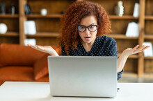 Puzzled And Confused Redhead Female Entrepreneur Staring At The Laptop Screen, Curly Woman In Shirt And Eyewear Looking At Monitor With Asking Expression, Misunderstanding What Happened