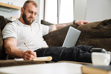 Wall Mural - White man with prosthesis writing down notes and using laptop