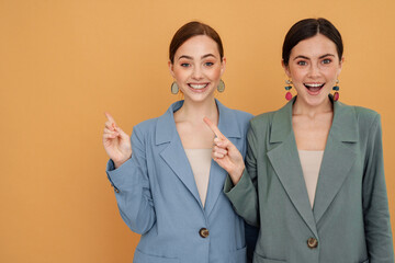 Young two women wearing jackets smiling and pointing fingers aside