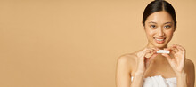 Website Header Of Portrait Of Adorable Young Woman Wrapped In Towel Smiling While Holding Lip Balm, Posing Isolated Over Beige Background