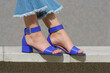 Women's legs in blue denim jeans and sandals in the city street. Trendy elegant casual outfit. Details of everyday summer look.