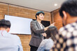business cooperation : Young asian male coach or speaker make flip chart presentation to diverse businesspeople at meeting in office. Male tutor or trainer present project to diverse colleagues.