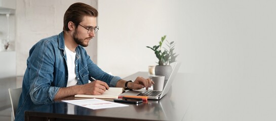 Happy young man sitting in home office and using laptop computer, smiling, chatting online