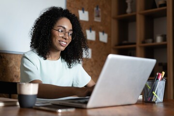 Poster - Young beautiful african american woman using her laptop while sitting in chair at her working place