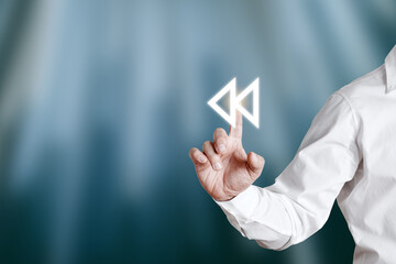 Businessman hand pressing rewind icon on a virtual display screen.