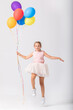 Sweet teenage girl holding a bunch of balloons jumps in an empty room, copy space on the empty wall