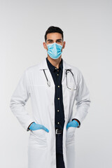 Poster - Arabian doctor in medical mask and latex gloves looking at camera isolated on grey