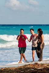 group of three people, two men and one woman, sharing and walking along the coast of cancun beach