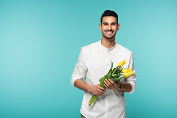 Canvas Print - Positive arabian man holding tulip flowers isolated on blue