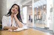 © kostikovanata - Cheerful business woman talking smartphone smiling having positive emotion at modern shopping mall